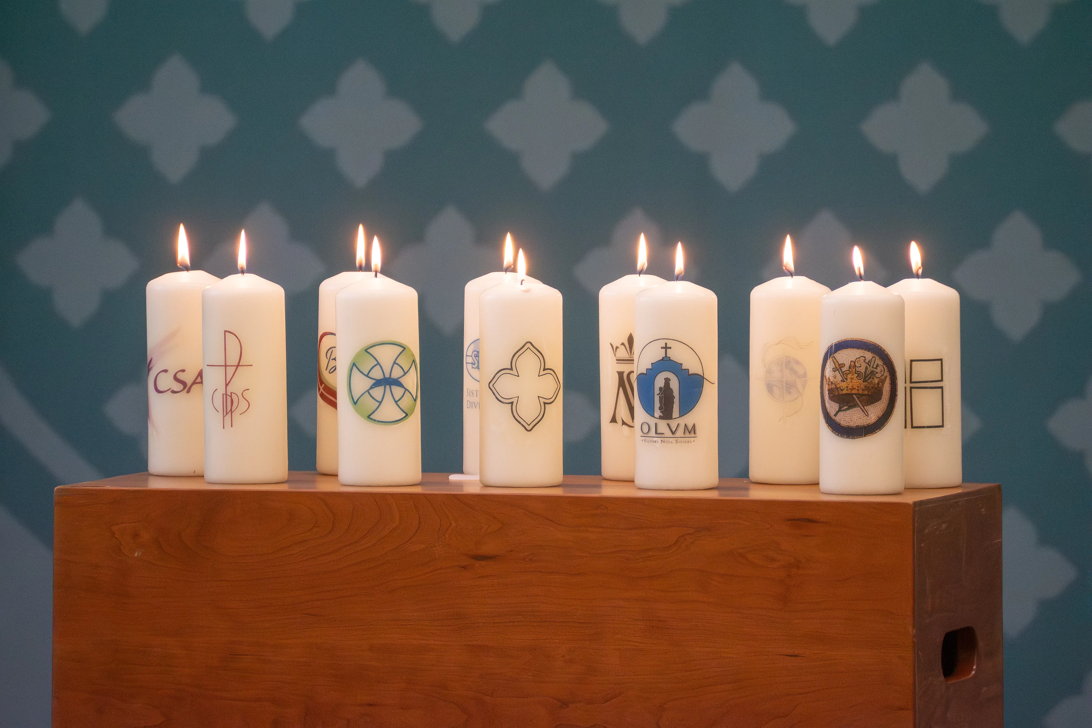 Row of lit pillar candles bearing the emblems of the ten congregations