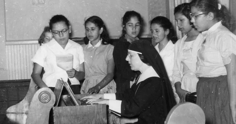 Archival photograph of a sister at a pipe organ with a group of students