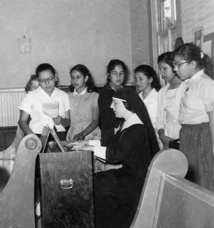 Archival photograph of a sister at a pipe organ with a group of students