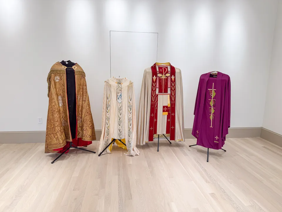 Four historic priestly vestments displayed on stands in a gallery